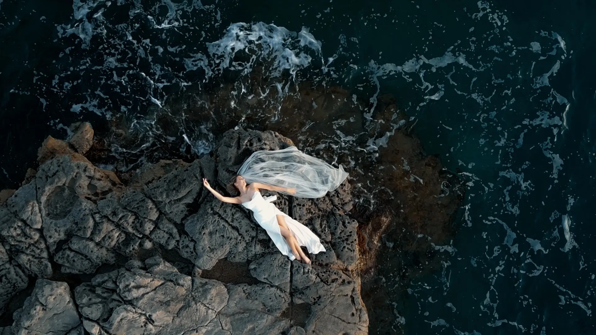 A bride lying on coastal rock, filmed from above